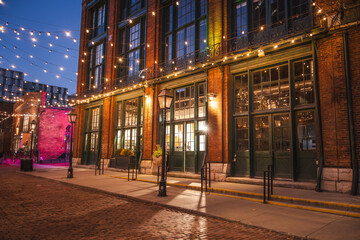 Fototapeta premium Evening view of historic brick buildings decorated with warm string lights in the Distillery District of Toronto, Canada.