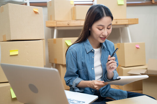 Young Asian woman owner of small online store packing customer orders in the home office.