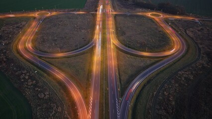 Aerial night view of highway interchange with roundabouts and light trails in rural Poland. Drone photo showing a symmetrical highway interchange with illuminated roundabouts and traffic light trails, © Marek