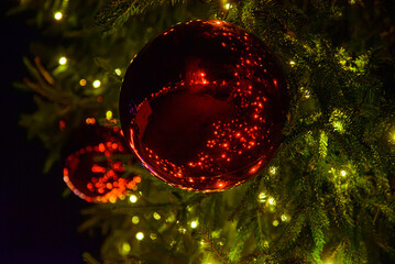 Close-up of a shiny red Christmas ornament on a decorated tree with warm glowing holiday lights in the background.