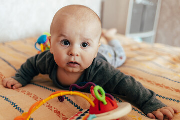 A baby lying on their stomach on a soft blanket reaches for colorful toys in a play area. Warm natural light and a cozy home environment create a bright and engaging family moment.
