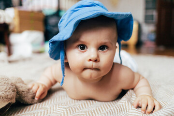 A baby lying on their stomach on a soft blanket reaches for colorful toys in a play area. Warm natural light and a cozy home environment create a bright and engaging family moment.