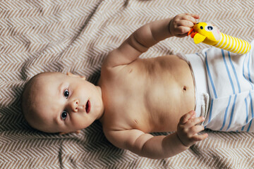 A baby lying on their stomach on a soft blanket reaches for colorful toys in a play area. Warm natural light and a cozy home environment create a bright and engaging family moment.
