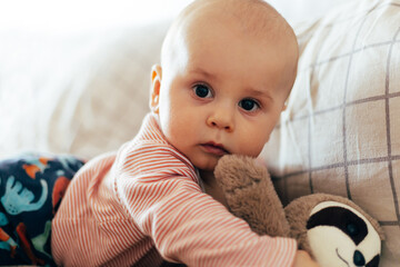 A baby lying on their stomach on a soft blanket reaches for colorful toys in a play area. Warm natural light and a cozy home environment create a bright and engaging family moment.
