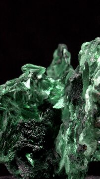 Malachite (green copper carbonate hydroxide) Fibrous chatoyant form giving cat's eye effect - rotating slowly against a black background. Vertical.