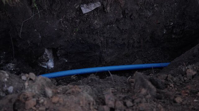 Excavation scene showing blue pipe in trench, camera gradually zooms in to reveal details of the surrounding earth and materials, emphasizing construction progress and environment