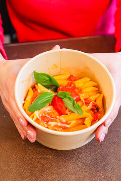 Pennetta al pomodoro fresco e basilico con grattugiata di formaggio servite in un contenitore da asporto di un take away e tenuto tra le mani di una cliente