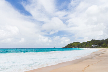Sunlit tropical beach with clear turquoise waves, soft sand, and distant green hills