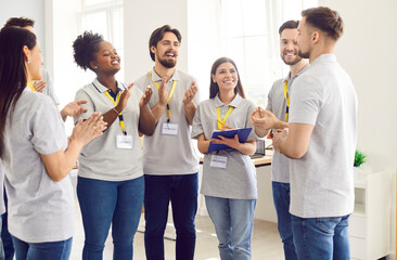 Group of happy diverse volunteers standing indoors, smiling and applauding finishing work in charity donation center. People volunteering in charitable foundation. Humanitarian aid concept.