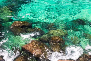 Fotobehang Zeegroen Bright turquoise water flows around rugged rocks, creating a vivid coastal scene  © evannovostro