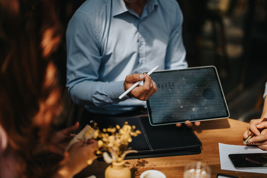 Two professionals share ideas at an outdoor cafe, using a tablet and stylus to review documents. A casual business meeting highlighting focus, collaboration, and modern work in a social setting.