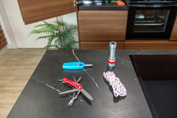 72 hour survival kit on kitchen counter including flashlight, rope, multitool knife and lighter, prepared for emergency situations and ensuring safety during natural disasters or unexpected events.