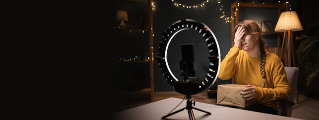 Female blogger unpacking box recording video using smartphone, ring light with tripod making wrong,...