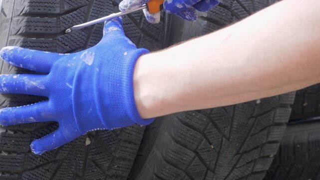 Worker hand in blue gloves pulls stones from wheel grooves. Autumn is moment for maintenance. Winter tread must stay open for stability. Safety on icy road begins with clean tire