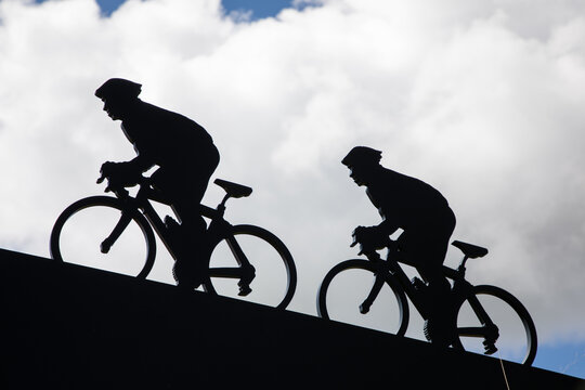 Fototapeta black silhouette of two cyclists ascending a hill against a cloudy sky man riding a bike