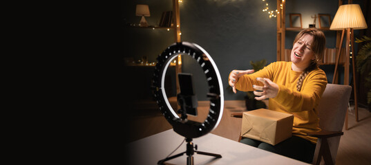 Evil Female blogger unpacking box recording video using smartphone, ring light with tripod...
