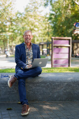 Fototapeta premium Senior man smiling, working outdoors with laptop in park