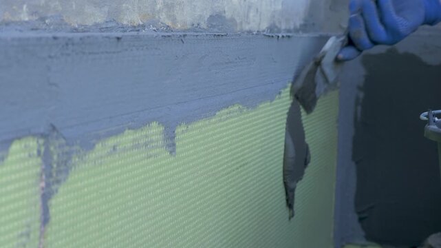 Worker plastering fiber glass mesh for exterior wall. Insulation system EWIS. Thermally insulated, protective exterior cladding procedure use expanded polystyrene, topped off plaster. Hand in gloves