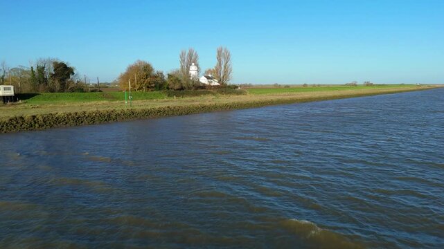 Cinematic aerial drone sweep approaching the historic Sir Peter Scott East Lighthouse beside the River Nene, revealing tidal wetlands and rural Lincolnshire landscapes.
