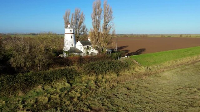 Cinematic aerial drone sweep approaching the historic Sir Peter Scott East Lighthouse beside the River Nene, revealing tidal wetlands and rural Lincolnshire landscapes.