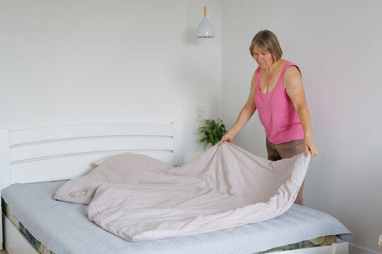 A woman is making her bed in a bright, inviting room. She is carefully adjusting the sheets and blankets, creating a neat and comfortable space