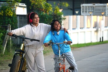 Obraz premium A woman puts her arm around the shoulder of the girl next to her, as they both stand with their bikes in a friendly and warm pose.