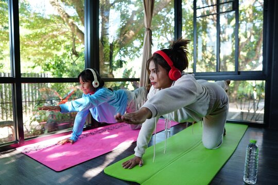 Two females performing the Bird Dog (Dandayamana Bharmanasana) or Table Pose Variation in yoga, wearing headphones while exercising.