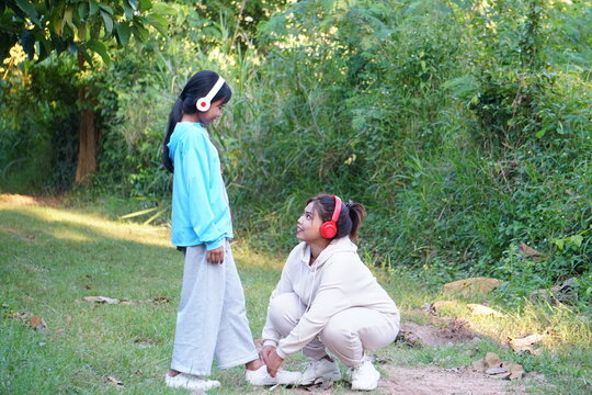The mother is crouching down to tie her daughter's shoelaces in the park.