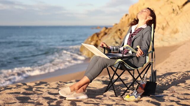 Businesswoman working on laptop and drinking whiskey on the seashore. Remote work concept. High quality 4k footage