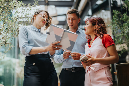 A group of colleagues in smart casual attire review a geometric chart together, sharing ideas and devices in a sunny, contemporary workspace.