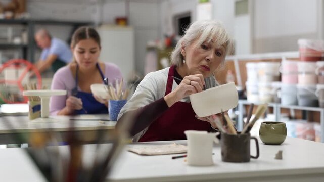 Woman potter with paintbrush, painting on plate in workshop, working in pottery studio