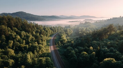 A railway line gently curves through a lush green forest at sunrise, enveloped in soft fog and illuminated by golden light, creating a serene and peaceful atmosphere
