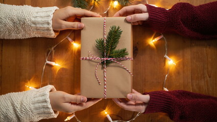 Warm holiday moment as two hands exchange a beautifully wrapped gift with festive decorations