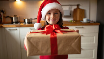 Child in Christmas hat presents holiday gift in cozy kitchen setting with warm lighting
