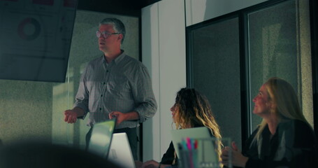 Male presenter pointing to chart on screen while team listens during modern office meeting with digital data visualization