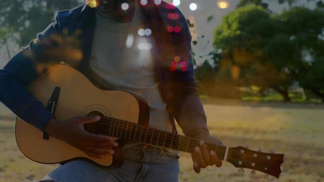 Male musician turning peg, strumming chords in park preparing music with layered bokeh overlay