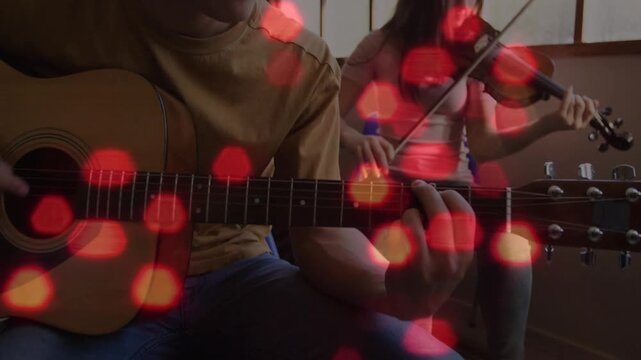 Camera pulling back, guitarist strumming and violinist bowing, rehearsing music under red bokeh