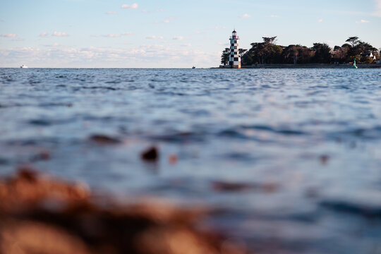 Low angle view across gentle sea waves toward a black and white lighthouse on distant shore, calm coastal landscape under soft blue sky.
Keywords (25)