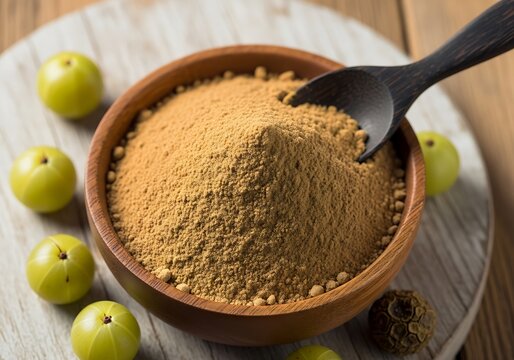 Close up of amla powder in a wooden bowl with fresh indian gooseberries and a wooden spoon on a board