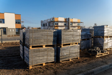 Pallets of gray paving stones wrapped in plastic on a dirt ground