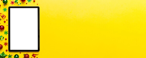 Christmas online shopping from home tablet pc with blank white display top view. Tablet with copy space on colored background with Christmas decorations balls,. Winter holidays sales background