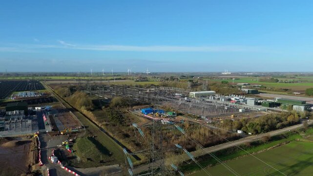 Aerial drone view of vast electrical substation with pylons, transformers, solar fields, wind turbines, and synchronous condensers in Walpole St Peter, UK