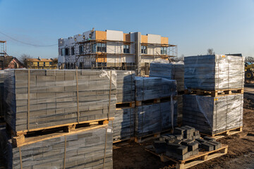 Pallets of gray paving stones wrapped in plastic on a dirt ground