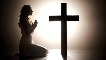 Woman kneeling in prayer before a glowing cross, spiritual contemplation