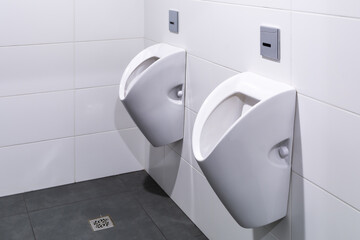 Modern White Urinals Mounted On Tiled Bathroom Wall In Public Restroom