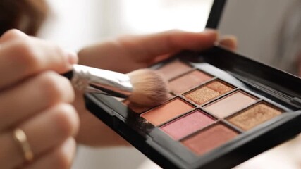 Woman's hand applying eyeshadow with a brush, beauty cosmetic routine - Powered by Adobe