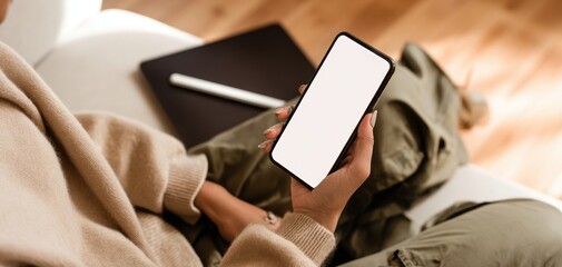 The smartphone with blank screen held by a relaxed person on a cozy sofa