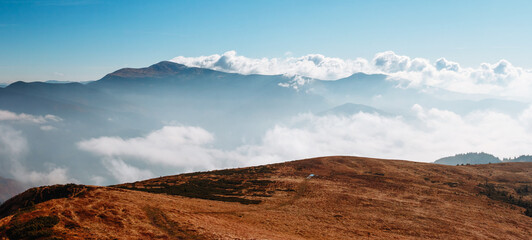 Breathtaking hilly landscape under clear blue skies with distant mountain ranges shrouded in soft mist shining at dawn. Magical atmosphere of Carpathian mountains.