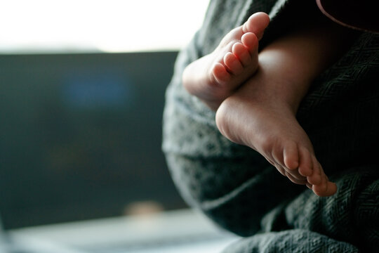 A close-up of a newborn tiny feet held in a parent hands while in a baby sling, emphasizing unity, love, and the emotional bond created through babywearing.