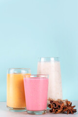 Autumn winter spicy fruit smoothie set. Various flavor tasty smoothie drinks in 3 glasses with yogurt, oats, seasonal fruits - apple, orange, cranberry, with anise and cinnamon